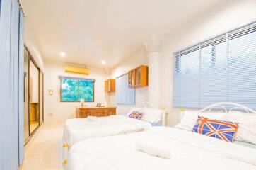 Bright modern bedroom with twin beds, window blinds, and wooden furniture.