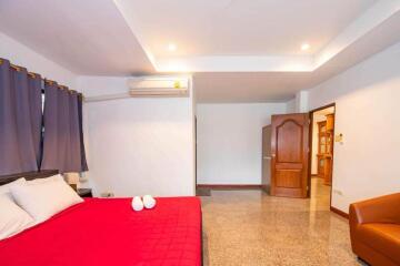 Spacious bedroom with red bedspread, air conditioning, and wooden door