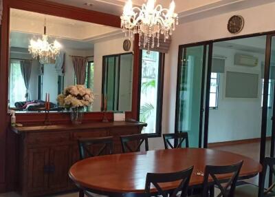 A elegantly furnished dining room with a wooden table, six chairs, chandelier lighting, mirror, decorative flowers, and sliding glass doors.