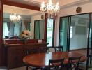 A elegantly furnished dining room with a wooden table, six chairs, chandelier lighting, mirror, decorative flowers, and sliding glass doors.