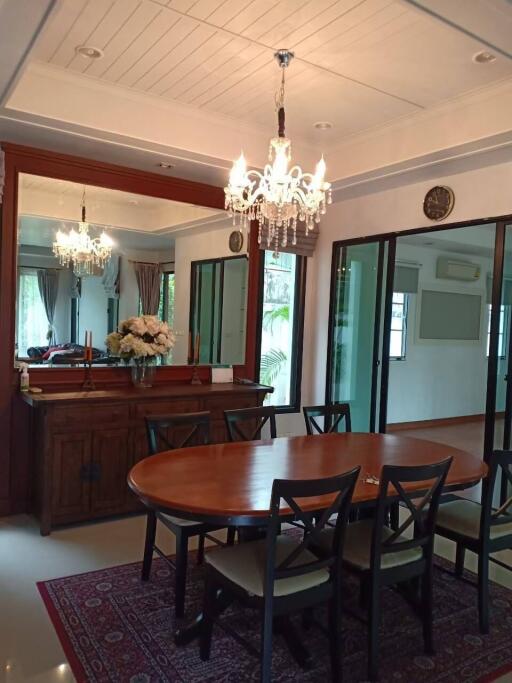A elegantly furnished dining room with a wooden table, six chairs, chandelier lighting, mirror, decorative flowers, and sliding glass doors.