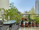 A spacious balcony with a glass table, wicker chairs, and various potted plants