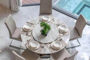 Elegant dining table set for six with a centerpiece, overlooking a pool