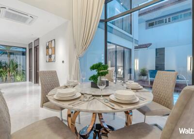 Elegant dining area with a round table set for a meal, large windows, and a view of the pool