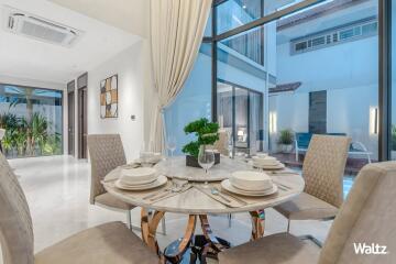 Elegant dining area with a round table set for a meal, large windows, and a view of the pool