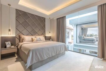 Modern bedroom with a large bed, decorative headboard, bedside tables, and a large window