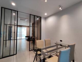 Modern dining room with glass table and beige chairs, view into living area