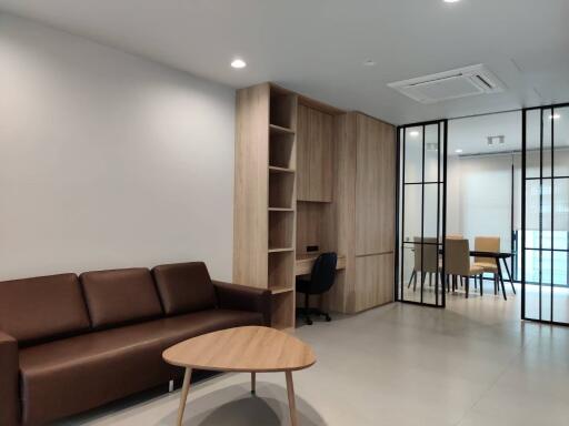 Modern living room with built-in wooden shelves, brown sofa, and adjoining dining area