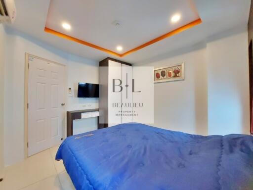 Modern bedroom with blue bedding, a wall-mounted TV, and a decorative ceiling