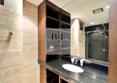 Modern bathroom with a large mirror, wooden shelving, and a sleek black countertop