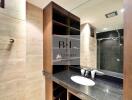 Modern bathroom with a large mirror, wooden shelving, and a sleek black countertop