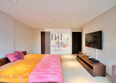 Spacious bedroom with large bed, wall-mounted TV, and modern decor