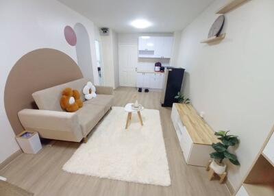 Modern and cozy living room with a beige sofa, wall art, a white rug, and open view into a kitchen area