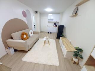 Modern and cozy living room with a beige sofa, wall art, a white rug, and open view into a kitchen area