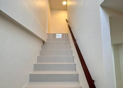 A view of a modern staircase with white walls and a wooden handrail.