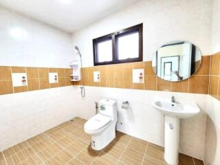 Well-lit modern bathroom with tiled walls, a round mirror, and a window