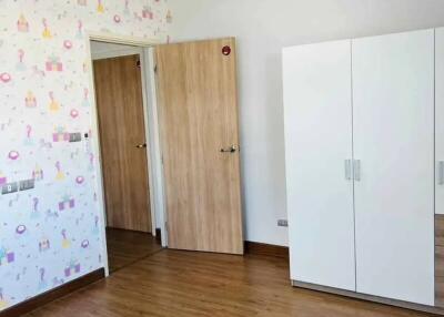 Empty bedroom with wooden floor, white wardrobe, and decorative wallpaper