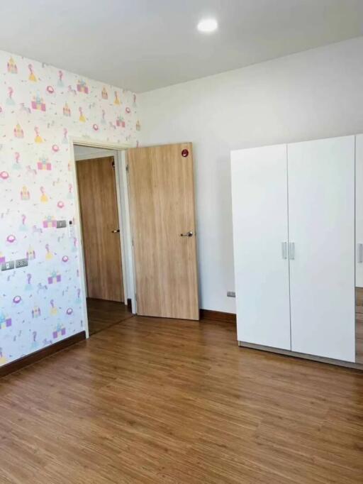 Empty bedroom with wooden floor, white wardrobe, and decorative wallpaper