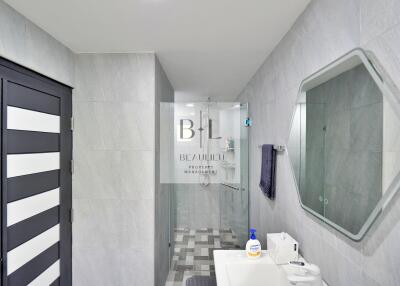 Modern bathroom with grey tile walls, walk-in shower, and hexagonal mirror