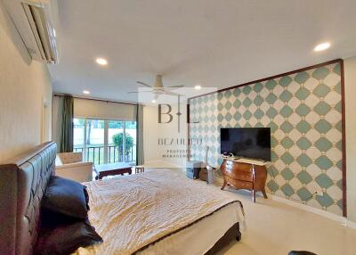 Spacious bedroom with large bed, wall-mounted TV, air conditioning, and sitting area by the window