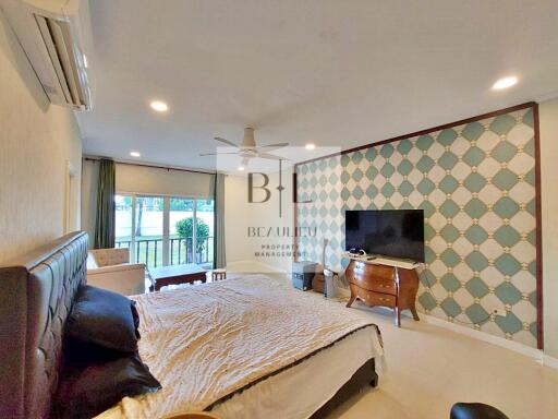 Spacious bedroom with large bed, wall-mounted TV, air conditioning, and sitting area by the window