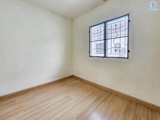 Empty bedroom with wooden flooring and window with metal bars