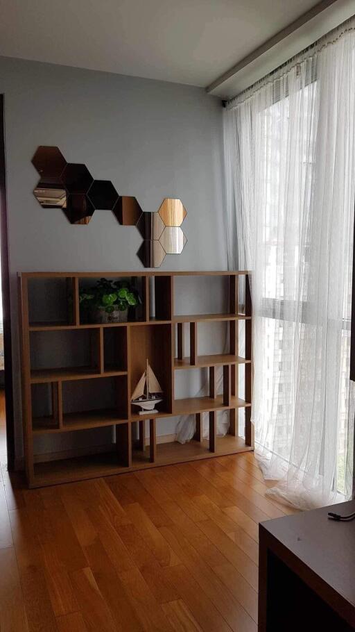 Living room with wooden floor, large window with sheer curtains, and decorative shelving unit