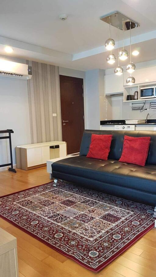 Living room with modern decor, black leather sofa, red cushions, patterned rug, and contemporary lighting