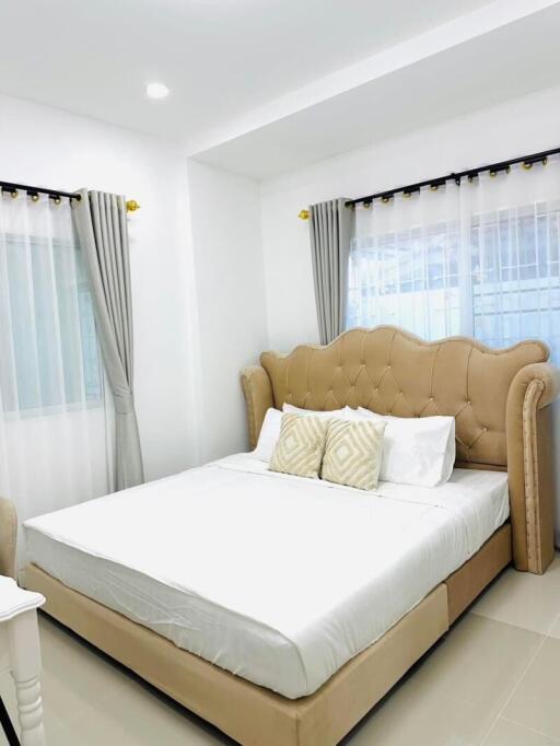 Bright and cozy bedroom with a cushioned beige bed and large windows with curtains