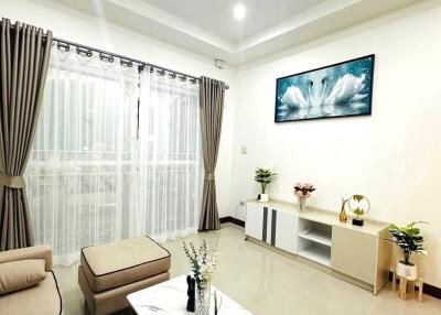 Spacious modern living room with beige furniture, a white coffee table, and large windows with curtains