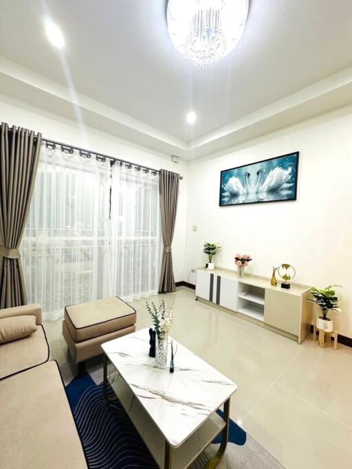 Spacious modern living room with beige furniture, a white coffee table, and large windows with curtains