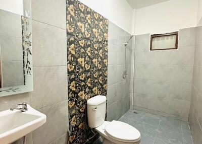 Modern bathroom with tiled walls and flooring, featuring a toilet, sink with mirror, and walk-in shower