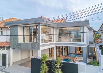 Modern two-story house with large windows, a balcony, and a pool