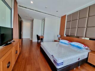 Modern bedroom with wooden floor, TV, bed, and desk