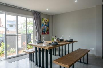 Modern dining area with wooden table and benches, set with dishes and glasses, and large windows letting in natural light