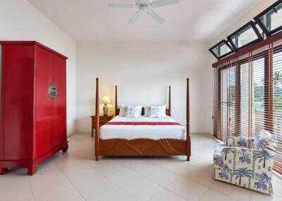 Spacious bedroom with large windows, bed, red wardrobe, and armchair