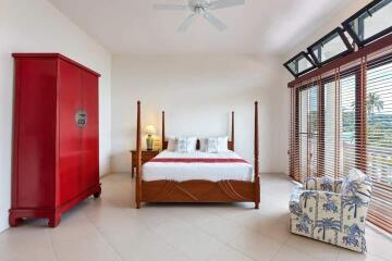 Spacious bedroom with large windows, bed, red wardrobe, and armchair