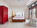 Spacious bedroom with large windows, bed, red wardrobe, and armchair