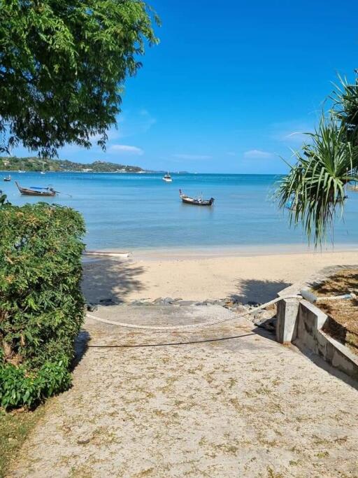 View of sandy beach and ocean with boats, surrounded by greenery.