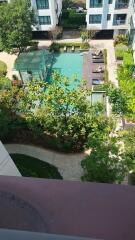 View of condominium pool area with lush greenery and surrounding buildings