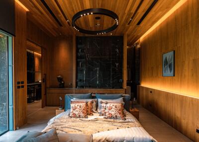 Modern bedroom with wooden ceiling and wall paneling, featuring a bed with decorative pillows, nightstands, ambient lighting, and an open view to the adjacent room.