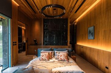 Modern bedroom with wooden ceiling and wall paneling, featuring a bed with decorative pillows, nightstands, ambient lighting, and an open view to the adjacent room.