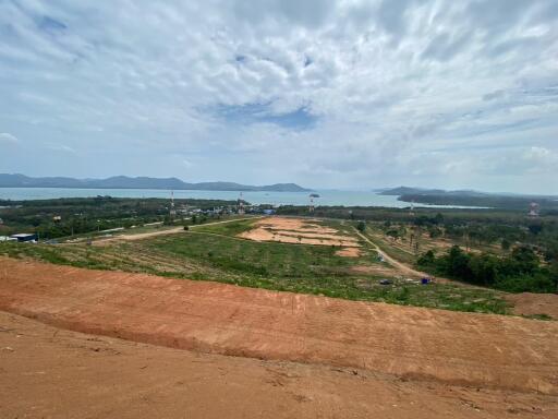 Scenic view of a landscape with cleared land, water body, and distant mountains under a partly cloudy sky