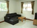 Cozy living room with large windows, a black sectional sofa, wooden coffee table, and TV corner.