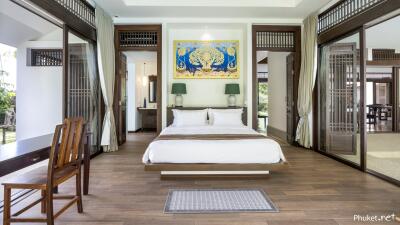 Spacious bedroom with a modern and luxurious design, featuring large windows, wooden furniture, and a decorative painting above the bed