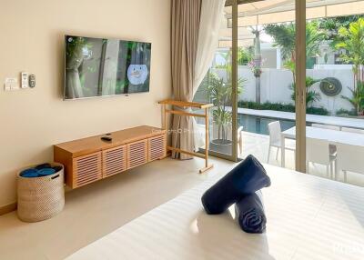 Modern bedroom with a TV on the wall, a view of the pool through large glass doors, and access to an outdoor seating area.