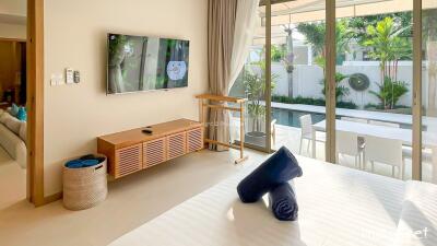 Modern bedroom with a TV on the wall, a view of the pool through large glass doors, and access to an outdoor seating area.