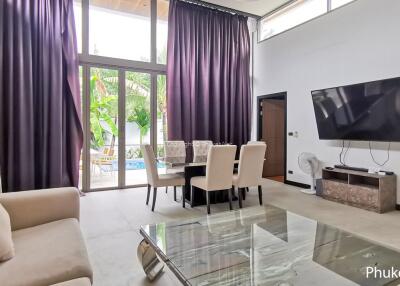 Living room with a large TV, dining table, and view of the outdoor pool area