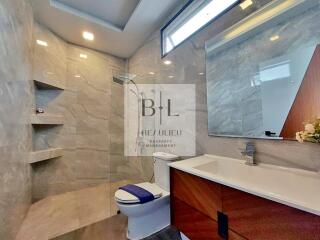 Modern bathroom with large mirror, wood accents, and walk-in shower.