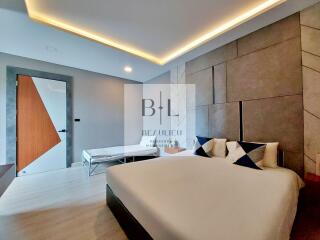 Modern bedroom with contemporary design featuring a bed, nightstands, geometric wall detail, and a seating area